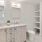 Large well lit bathroom with large mirror and white cabinets with a spacious walk in closet.